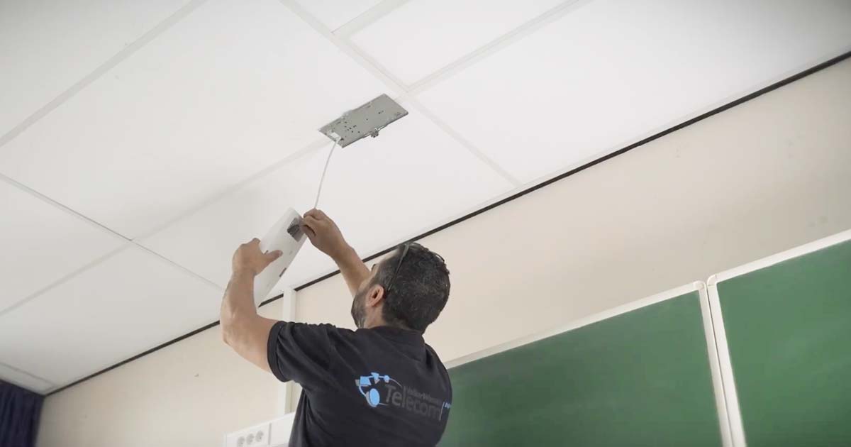 Un installateur place une borne Wifi dans une classe de cours.